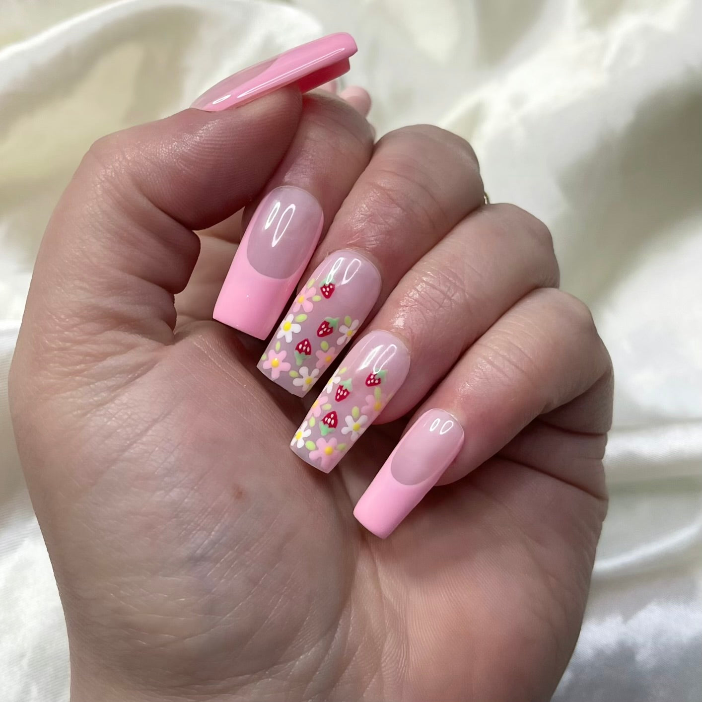 Strawberry Patch press-on nails feature rosy pink French tips, white and pink flowers, golden centres, hand-painted strawberries, and soft pinky nude bases for a fresh, fruity spring look.